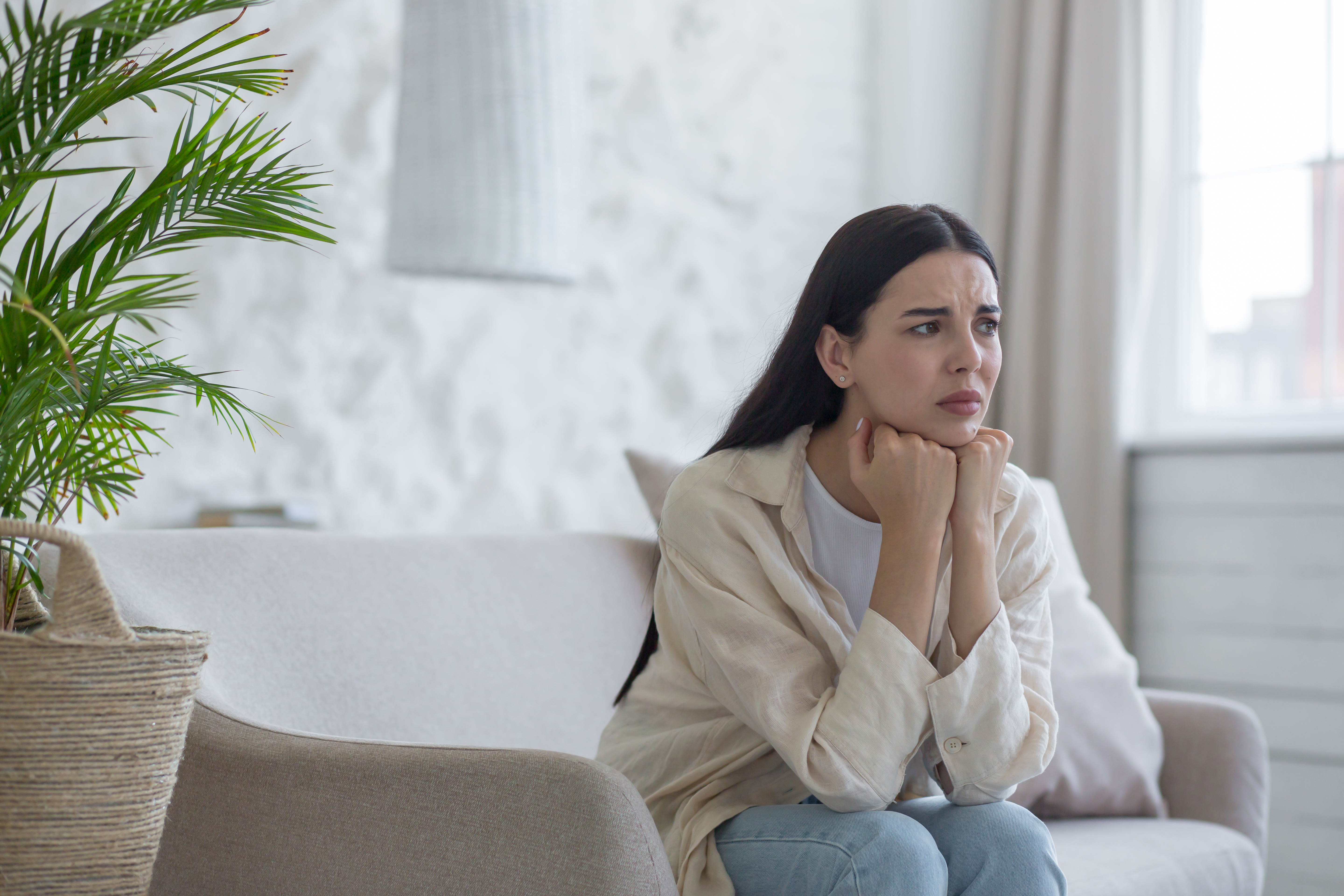 A sad and disappointed woman is alone at home sitting on the couch in depression, thinking